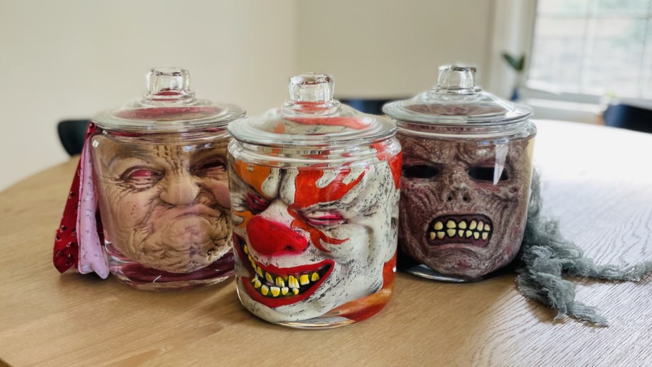 creepy halloween decorations - face masks in clear glass jars on wood table